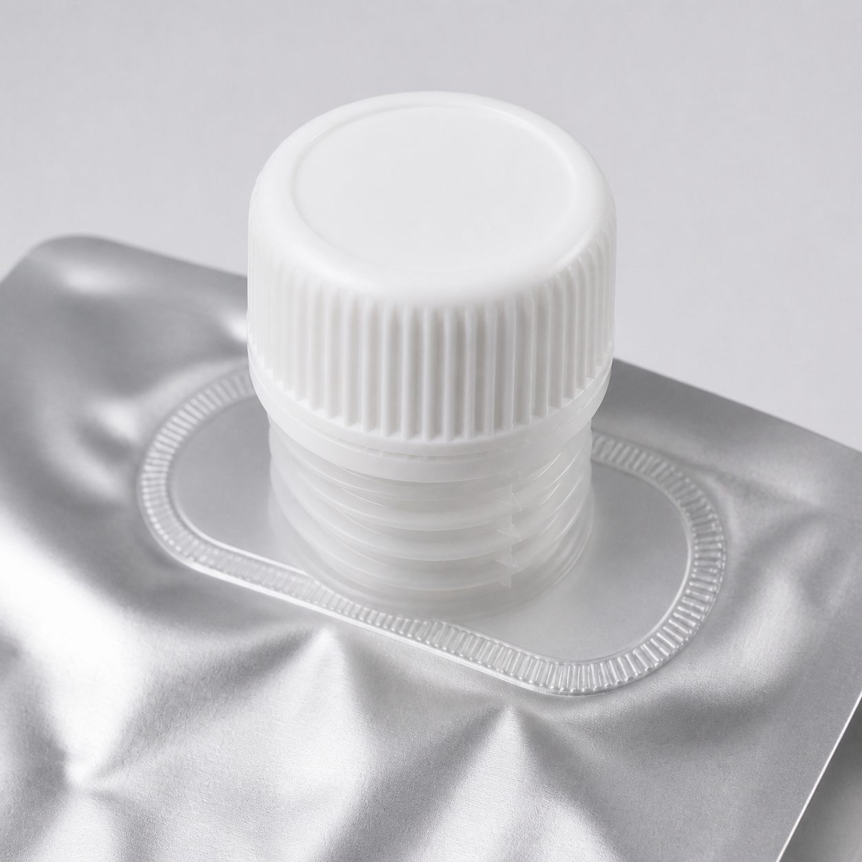 Close-up of a threaded spout, screw cap, and welded flange on silver barrier film for compatibility review
