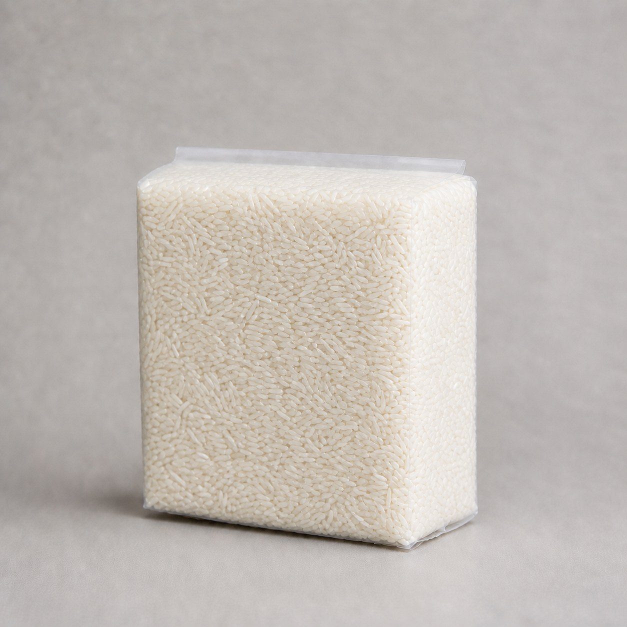 Transparent vacuum-sealed rice brick showing natural long-grain white rice, tight film and a short horizontal heat-seal fin